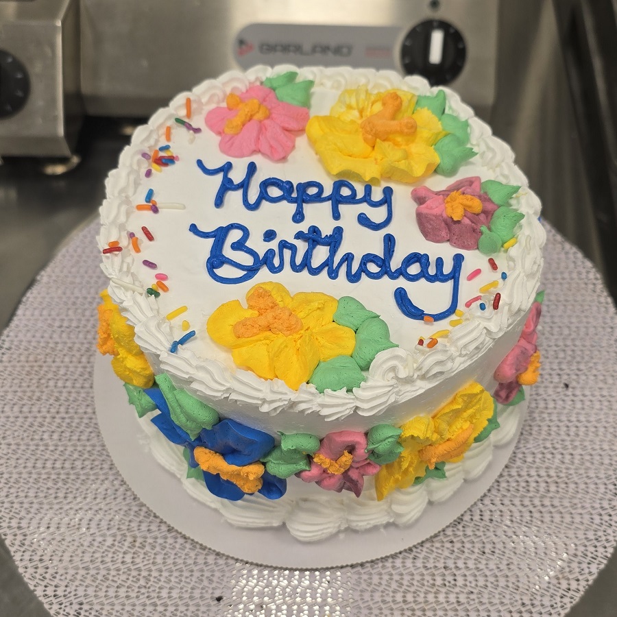 Cake that says Happy Birthday and is covered with piped flowers of many colors.